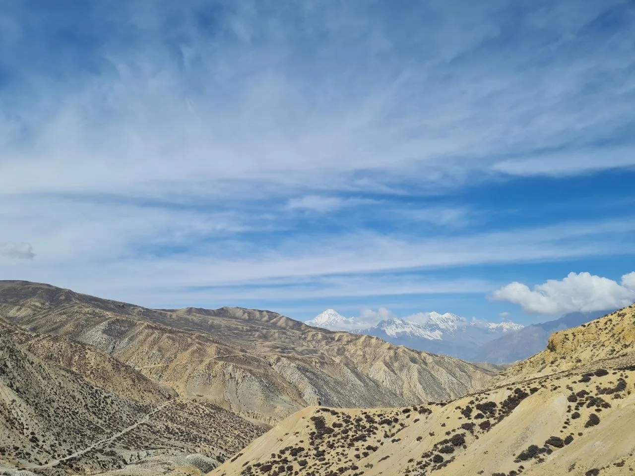 Arid Mustang plateau ridgelines with snow-capped Himalayan peaks visible on the horizon.