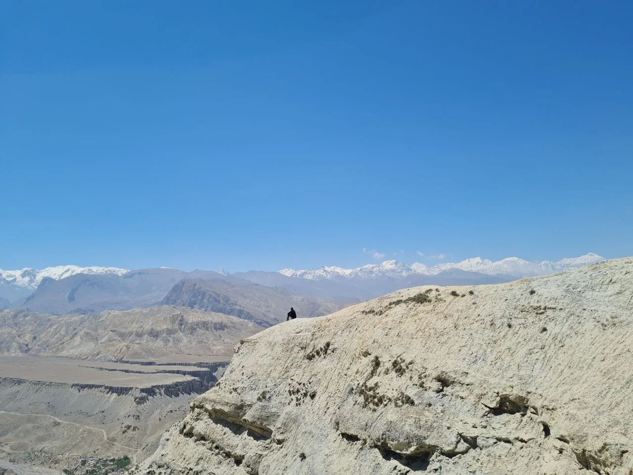Hiker rests on an eroded cliff edge overlooking the arid Mustang valley, Nepal.