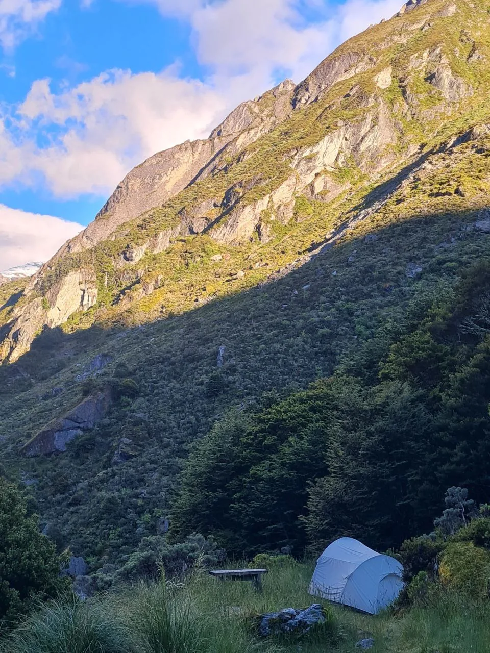 A solo tent pitched at a Rees-Dart campsite beneath steep alpine cliffs.